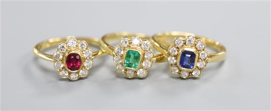 Three modern 18ct gold and gem set cluster rings, to include, emerald, ruby and sapphire,